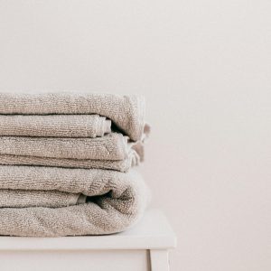 Stack of soft clean fresh gray towels placed on white minimalist stool against beige wall